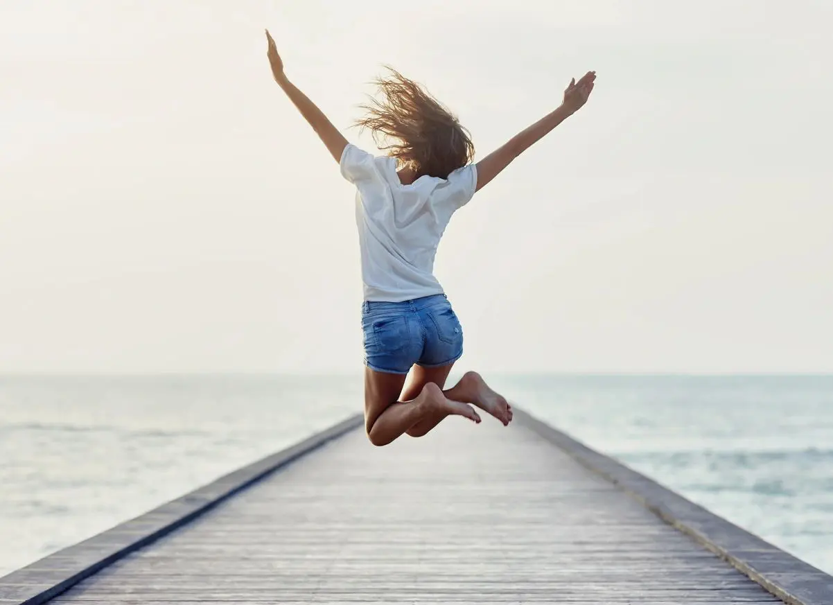 A woman jumping in the air on top of a pier.